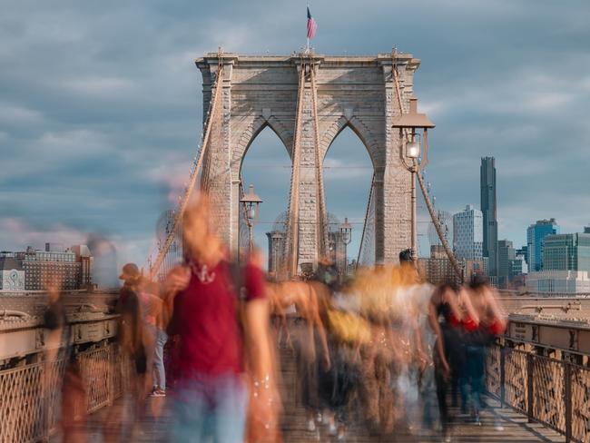 Walkway across Brooklyn Bridge in New York with a crowd of blurred tourists passing by.