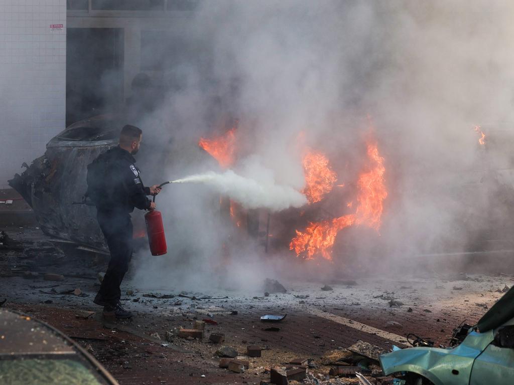 A member of Israeli security forces tries to extinguish fire on cars following a rocket attack from the Gaza Strip in Ashkelon. Picture: AFP