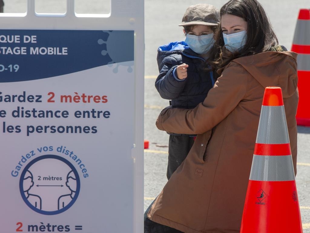 A woman and child wait for a test in Montreal. One expert said in the case of flu, targeting children is actually the best way to stop a virus spreading. Picture: Ryan Remiorz/The Canadian Press via AP.