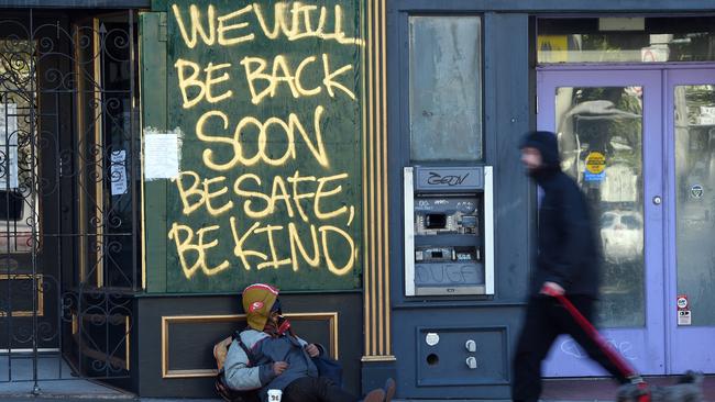 A man walks his dog past a homeless man sleeping under a message painted on a boarded up shop in San Francisco, California. Picture: Josh Edleson/AFP