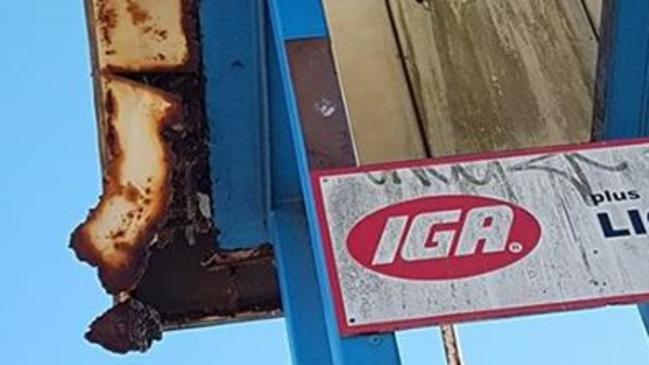 A rusted piece of metal hangs from the Airds Village Shopping Centre sign.