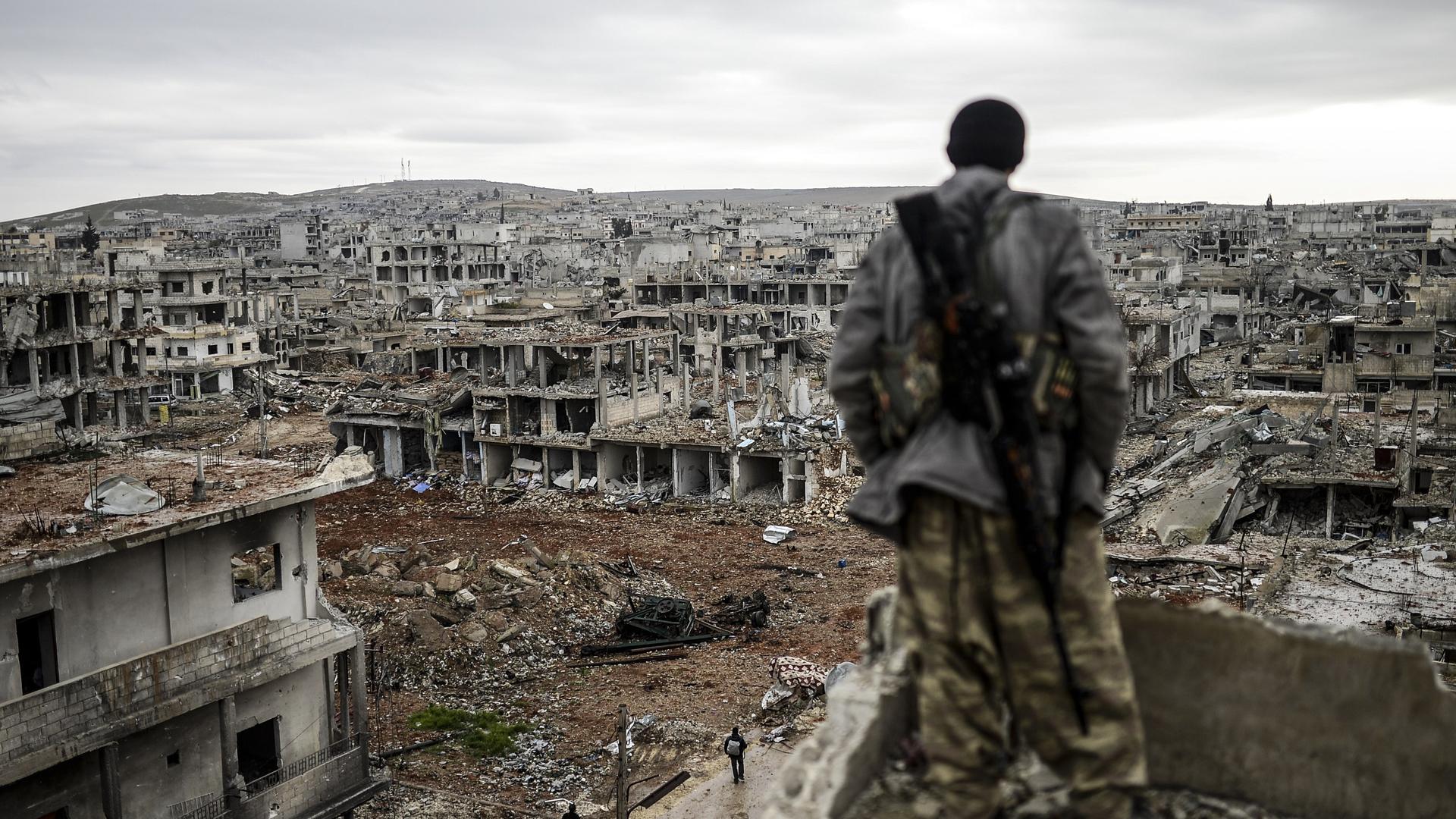 -- AFP PICTURES OF THE YEAR 2015 -- Musa, a 25-year-old Kurdish marksman, stands atop a building as he looks at the destroyed Syrian town of Kobane, also known as Ain al-Arab, on January 30, 2015. Kurdish forces recaptured the town on the Turkish frontier on January 26, in a symbolic blow to the jihadists who have seized large swathes of territory in their onslaught across Syria and Iraq.     AFP PHOTO/BULENT KILIC