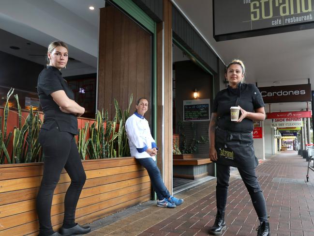 LtoR Staff members, Nelle, Chef Daniela, and Fi, outside of The Strand restaurant, showing relatively empty Jetty Road in background. The tourist strip has been described as a ghost town because of coronavirus, and the Grand hotel closing, will further affect the precinct. Strand says trade is down 80 per cent - the owner is paying staff from his own pocket to continue trading as takeaway. Picture Dean Martin