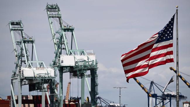 The US flag blows in the wind as cranes stand above cargo shipping containers on ships at the Port of Los Angeles. Picture: Patrick T. Fallon / AFP