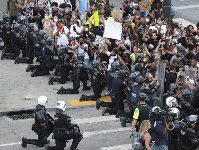 In a show of peace and solidarity, law enforcement officials with riot shields take a knee in front of protesters in Atlanta. Picture: AP