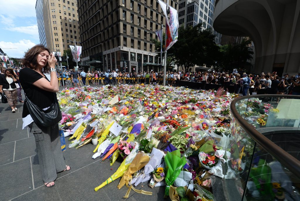 A visitor looks at a makeshift memorial near the scene of a fatal siege in the heart of Sydney's financial district on December 16, 2014. Sydneysiders including tearful office workers and Muslim women in hijabs laid flowers at the scene of the deadly siege, in an outpouring of grief and shock that this could happen in their easy-going city. AFP PHOTO/Peter PARKS. Picture: PETER PARKS