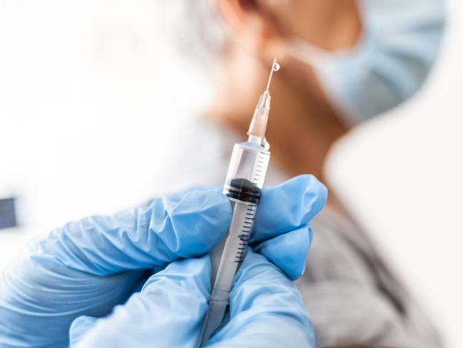 Photo of male nurse wearing protective face mask and gloves preparing medical syringe for giving injection to senior patient Picture: Istock