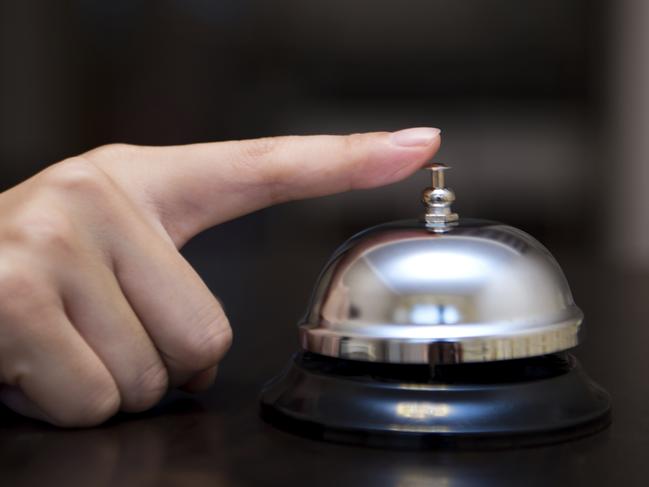 Hand ringing in service bell on wooden table.