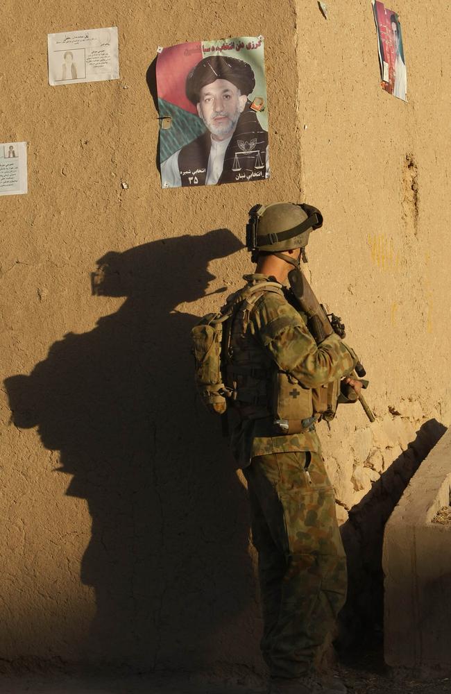 A poster of President Hamid Karzai above an Aussie digger on patrol in the township of Merwais in southern Afghanistan. The president would complain about night operations on townships. Picture: Supplied