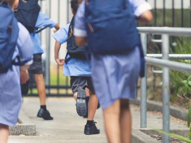 School children running away. They are wearing uniforms and carrying backpacks. They are having a race. Multi ethnic group with Asian, Caucasian and Aboriginal children. Rear view