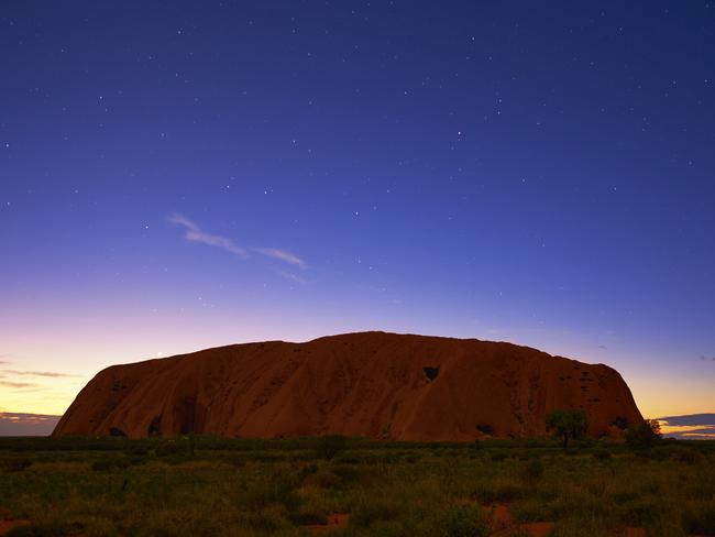 Northern Territory, Australia - March 29, 2016: Pre-dawn in the heart of the Australian Outback, and countless stars overhead gently illuminates the massive form of Uluru that looms majestically on the horizon.