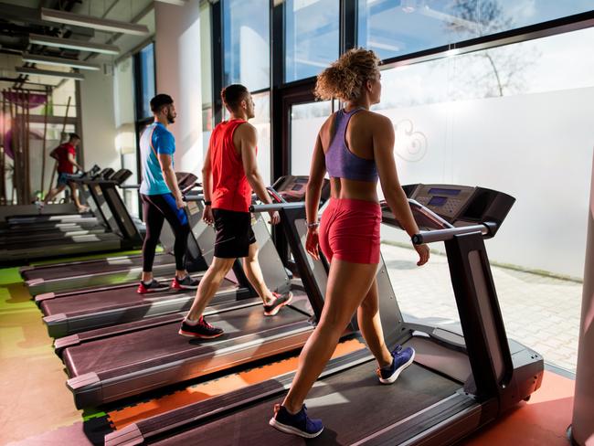 Team of young people exercising in health club while walking on treadmills.  Focus is on young woman.