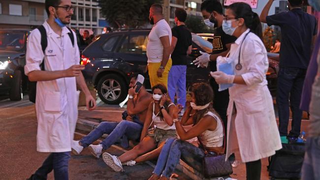 People injured in the Beirut explosion sit on the pavement outside a hospital as medics walk past. Picture: AFP