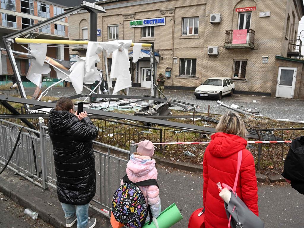 People are seen outside the cordoned off area around the remains of a shell in a street in Kyiv on February 24, 2022.