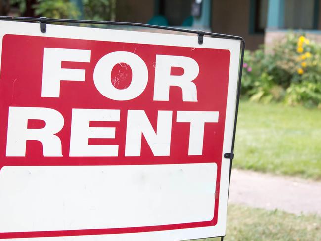 A blank red and white for rent sign is posted in the front yard of a home. The home has a porch and is a rental property.