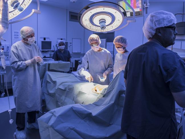 Surgical team performing operation in hospital operating room. Medical team with patient on operating table with surgical lights above. Istock