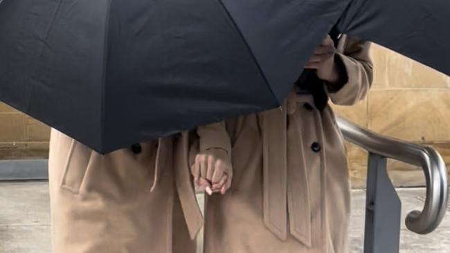 Grace and Lara Buttriss don matching outfits while hiding behind an umbrella exiting Picton Courthouse on August 19, 2022. Picture: Annie Lewis