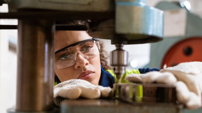 Close-up of female apprentice using yoke machine. Female engineer is wearing protective glasses in factory. She is working in manufacturing industry.