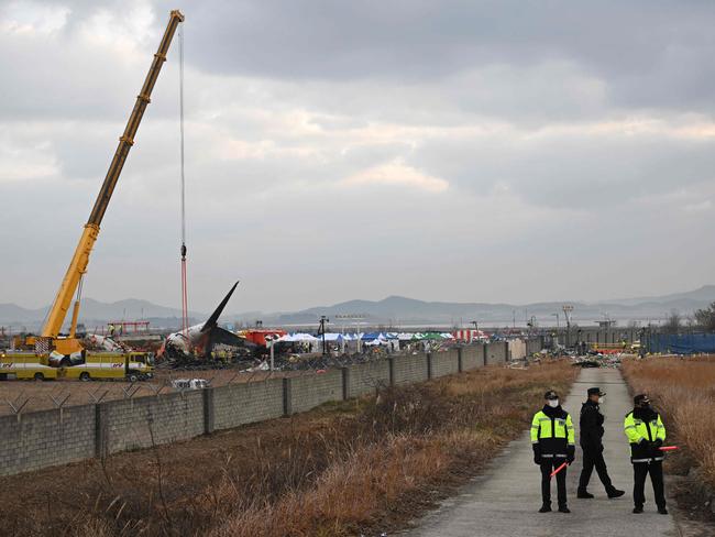 Police officers stand guard as firefighters and recovery teams work at the scene where a Jeju Air Boeing 737-800 series aircraft crashed and burst into flames at Muan International Airport in Muan, some 288 kilometres southwest of Seoul on December 30, 2024. The Boeing 737-800 was carrying 181 people from Thailand to South Korea when it crashed on arrival on December 29, killing everyone aboard -- save two flight attendants pulled from the twisted wreckage of the worst aviation disaster on South Korean soil. (Photo by JUNG YEON-JE / AFP)