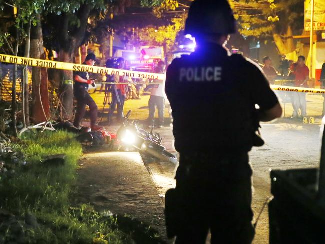 In this Friday, Sept. 23, 2016 photo, a police SWAT member stands guard as police operatives examine the scene where two bodies lay on a road after being killed in a police drug 