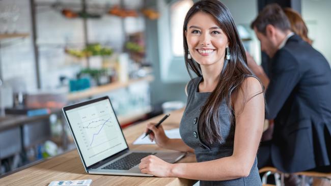 Happy business woman working at a cafe on a laptop and looking at the camera smiling. Image on screen is own design. Investor generic