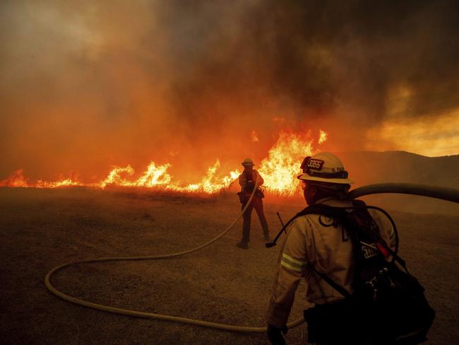 Firefighters spray water as they monitor flames caused by the Hughes Fire along a roadside in Castaic, California. Picture: AP