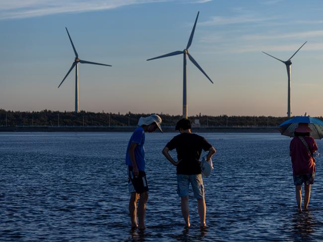 TAICHUNG, TAIWAN - AUGUST 22: Wind turbines stand behind visitors at Gaomei wetland during sunset on August 22, 2024 in Taichung, Taiwan. Taiwan, a leader in utilising natural resources for power, is rapidly expanding its wind power generation, particularly through offshore projects, to meet its renewable energy targets. By 2025, the government aims for wind energy to contribute 3 GW to its goal of 10 GW from renewable sources, leveraging the island's strong wind resources and favorable conditions for offshore developments. (Photo by Annabelle Chih/Getty Images)