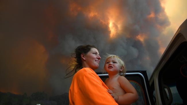 Sharnie Moren and her 18 months old daughter Charlotte look on as thick smoke rises from bushfires near Nana Glen, near Coffs Harbour, Tuesday, November 12, 2019. There are more than 50 fires burning around the state, with about half of those uncontained. (AAP Image/Dan Peled) NO ARCHIVING