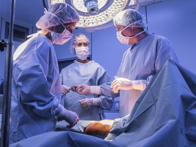 Doctors wearing surgical masks and gowns performing an operation on patient in hospital operating theater.