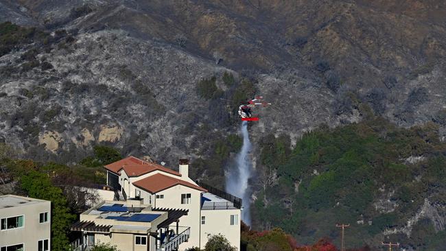 A CalFire helicopter drops water next to a building near hillsides scorched by the Palisades Fire in Fernwood, Topanga, a community in western Los Angeles County. Picture: AFP