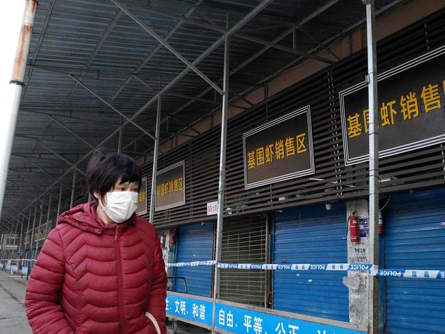 (FILES) This file photo taken on January 12, 2020 shows a woman walking in front of the closed Huanan wholesale seafood market, where health authorities say a man who died from a respiratory illness had purchased goods from, in the city of Wuhan, Hubei province. - January 11, 2021 marks the anniversary of China confirming its first death from the Covid-19 coronavirus -- a 61-year-old man who was a regular at the now-notorious Wuhan wet market linked to many of the early cases. (Photo by Noel Celis / AFP)