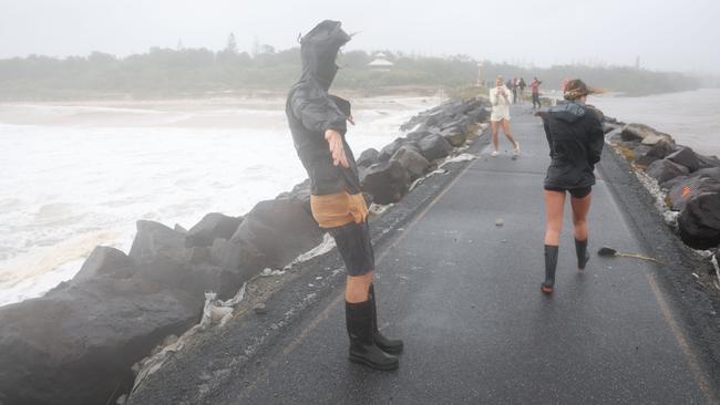 People walk out on the Brunswick Heads break wall and lean into the wind on Friday, as the Far North Coast continues to cop a battering. Picture: Rohan Kelly