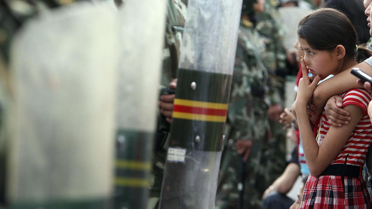 An Uighur girl is stopped by a line of riot police officers in Urumqi, the capital of western China’s Xinjiang province.