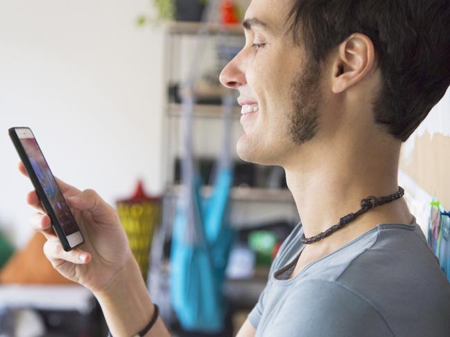 Whatsapp or tinder date. Young caucasian man smiling while using a smartphone at home