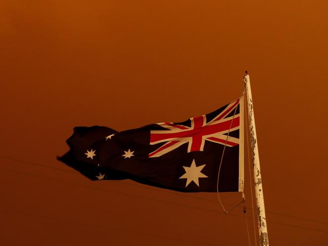 The Australian flag flies under red skies from bushfires in East Gippsland, January 4, 2020. The bushfire crisis has tested us in extraordinary ways, writes Ken Wyatt. Picture: Darrian Traynor/Getty Images