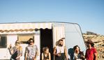 Group of young people alternative millennial young men and women standing outside a vintage caravan enjoying the sunny day of summer outdoor leisure activity together in friendship