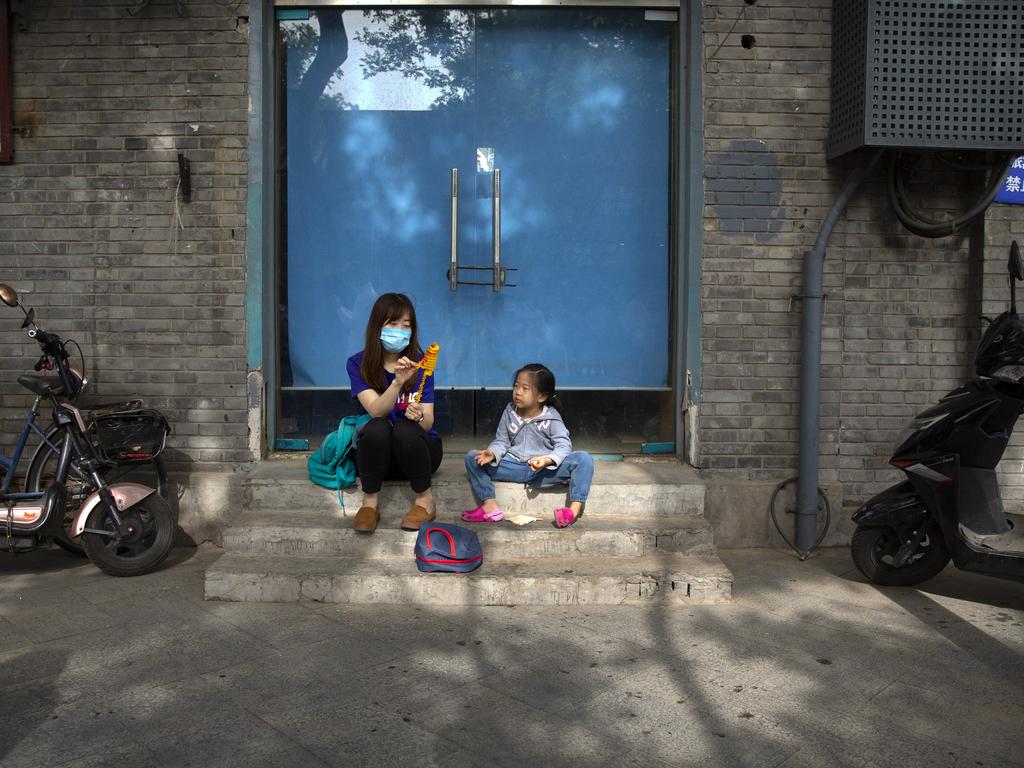 A woman shares a snack with a girl as they sit on a pedestrian shopping street in Beijing. Picture: Mark Schiefelbein