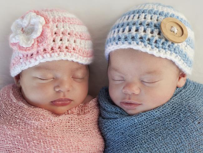 Five week old sleeping boy and girl fraternal twin newborn babies. They are wearing crocheted pink and blue striped hats.