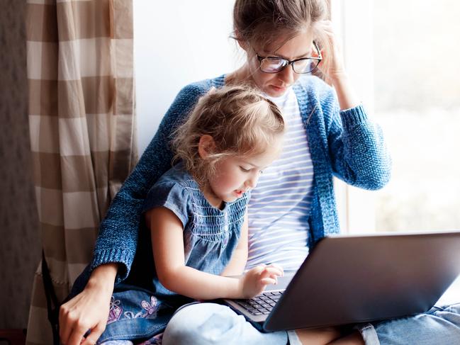 CORONAVIRUS: Picture: istock Working mom works from home office with kid. Mother and daughter read news. Woman and cute child sitting on window sill. Freelancer workplace with laptop and the Internet. Female business, career.