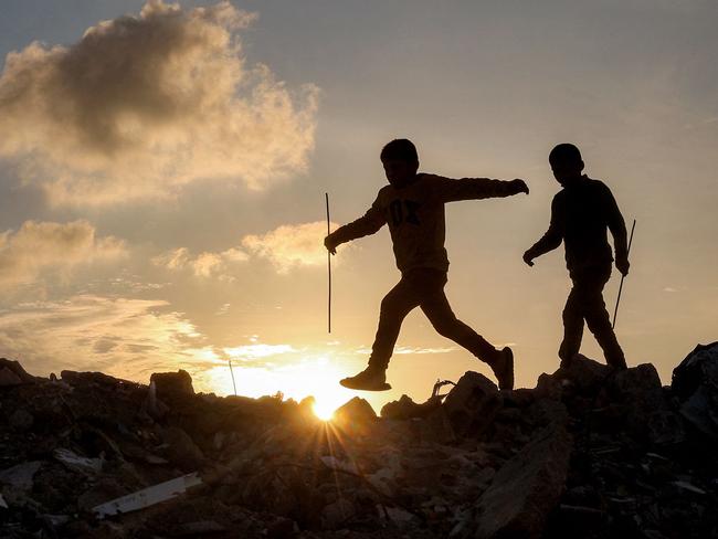 TOPSHOT - Boys walk atop a mound of rubble at a camp for people displaced by conflict in Bureij in the central Gaza Strip on January 17, 2025 following the announcement of a truce amid the ongoing war between Israel and Hamas. (Photo by Eyad BABA / AFP)