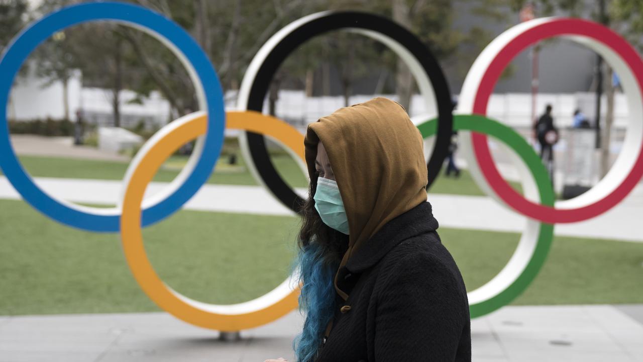 A woman wearing a face mask walks past the Olympic rings in front of the new National Stadium in Tokyo.
