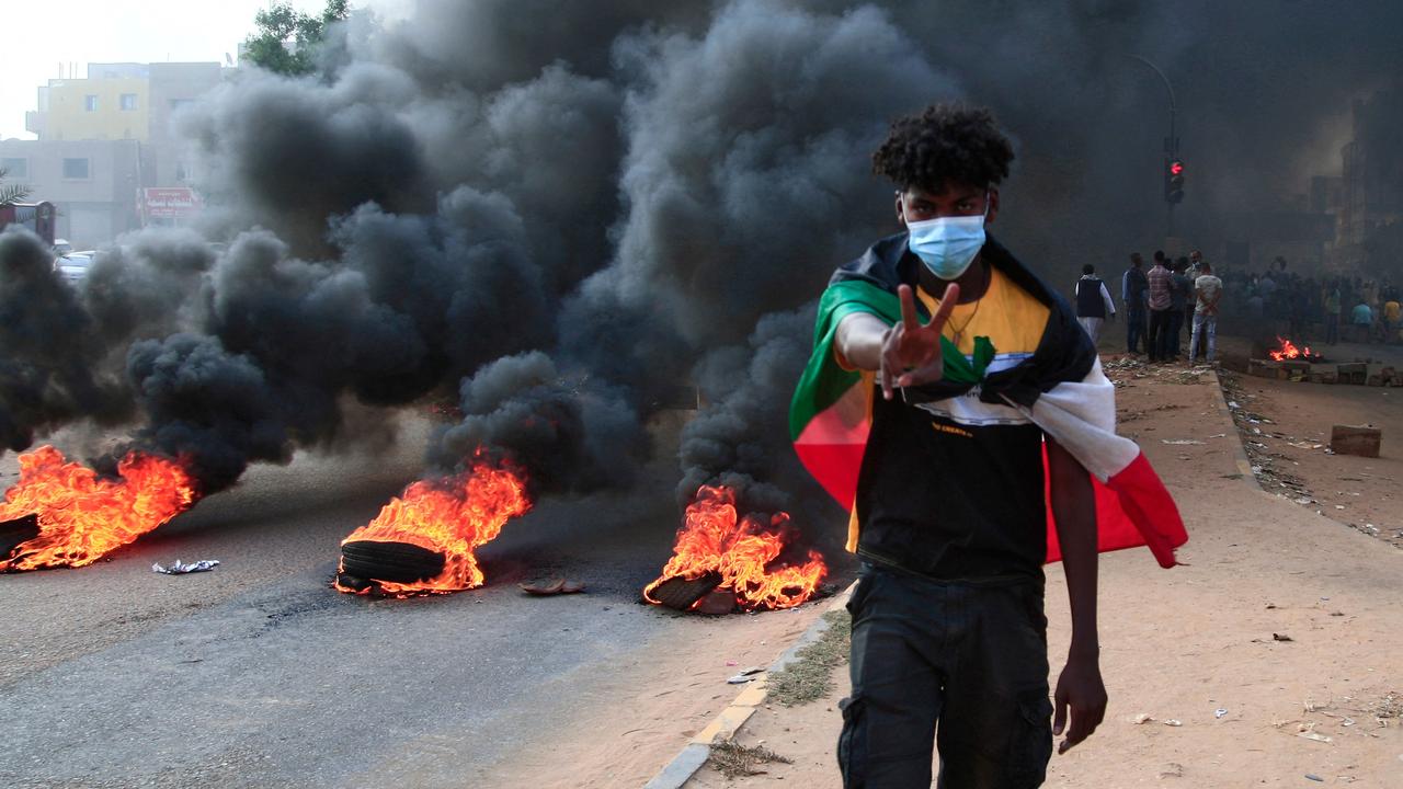 A protester draped with the Sudanese flag flashes the victory sign next to burning tyres during a demonstration in the capital Khartoum. Picture: AFP