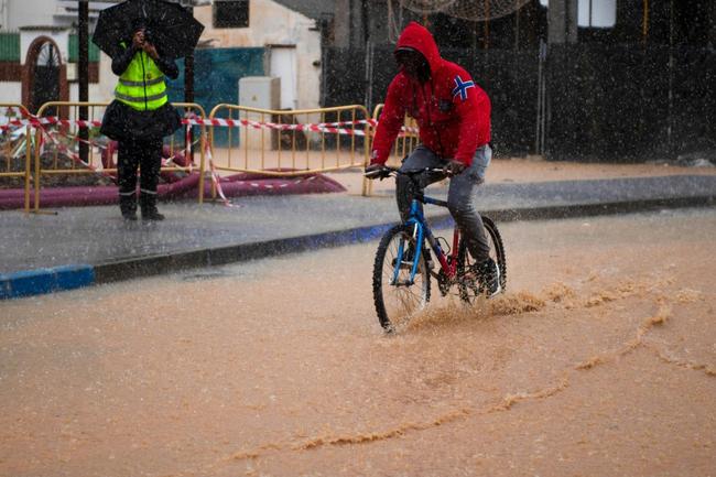 A man rides a bicycle down a flooded street in Campanillas, near Malaga, on November 13, 2024