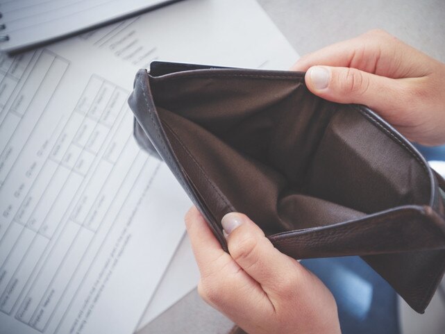 Woman opening an empty wallet. There is paperwork on the desk in the background. Poverty, budget and overspending concept. Photo: iStock