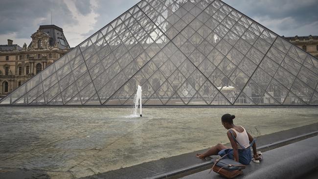 A Parisian relaxes next to the water fountain at the Louvre Museum. Picture: Getty Images