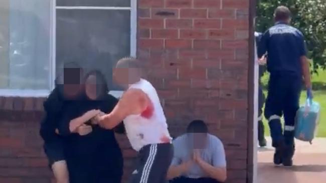 Two men, one with blood on his singlet help a woman after two people were injured in a stabbing. Picture: Supplied