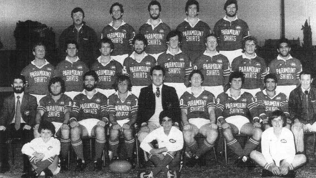 Reclusive radio station owner Bill Caralis is seated centre in a suit and flanked by league legends Tommy Raudonikis and Phil Gould. 