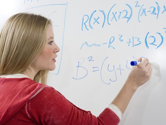 Female student writing maths equations on whiteboard.