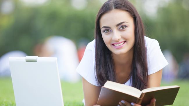 Brunette girl with notebook and book on green grass in the park. To illustrate online study. iStock image