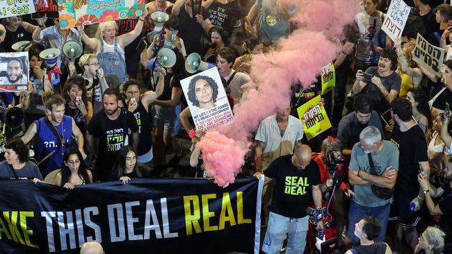 A demonstrator lights a pink flare as others deploy a banner and raise pictures of hostages during an anti-government protest in Israel. Picture: AFP